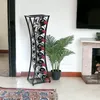 A black metal wine rack filled with wine bottles stands next to a potted plant in a room with a fireplace and a rug. Podgląd zdjęcia produktu