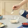 A hand is adding powder from a scoop into a glass bowl. Produktbild-Vorschau