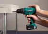 A person is using a green and black cordless drill to screw into a light-colored wooden surface. Produktbild-Vorschau