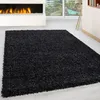 A black shaggy rug in a modern living room with a fireplace and large windows. Produktbild-Vorschau