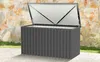 A dark gray storage box with its lid open, placed on a concrete patio next to a stone wall and some greenery. Produktbild-Vorschau