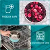 The image is a collage showing two distinct scenarios: the top half displays a bowl of frozen berries on ice cubes with the text 'FREEZER SAFE', and the bottom half shows a hand placing a blue stainless steel bowl into a dishwasher with the text 'DISHWASHE Produktbild-Vorschau