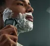 A man is shaving his face with an electric razor covered in shaving cream. Náhled obrázku produktu