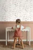 A young girl sits at a white desk in front of a floral wallpaper. Podgląd zdjęcia produktu