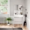 A white vanity table with a mirror and makeup accessories in a room with a window and a plant. Podgląd zdjęcia produktu