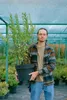 A man stands in a greenhouse holding a potted plant. Produktbild-Vorschau