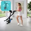 A woman is exercising on a stationary bike in a bright, modern room with large windows overlooking a garden. Anteprima dell’immagine prodotto