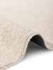 A close-up view of a cream-colored rug, showing its textured surface and a curled edge. Voir les images du produit