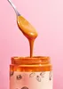 A close-up shot of peanut butter being scooped from a jar against a pink background. Produktbild-Vorschau