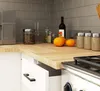 A close-up shot of a kitchen countertop with various items, including a coffee maker, jars, oranges, and spice containers. A partially open drawer is also visible. Produktbild-Vorschau