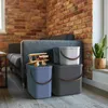 Three storage boxes are stacked in a living room setting, with a couch and brick wall in the background. A wooden toy airplane sits on top of the front box. Produktbild-Vorschau