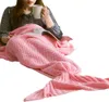 A person is sitting wrapped in a pink mermaid tail blanket, holding a mug and reading a book. Produktbild-Vorschau