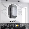 A modern bathroom with a marble-tiled wall, featuring an oval LED mirror with integrated lighting. Below the mirror are black faucets and a dark vanity. The bottom of the image displays icons and text highlighting product features. Produktbild-Vorschau