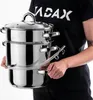 A person is holding a multi-tiered stainless steel pot with a glass lid and a clear tube attached. Produktbild-Vorschau
