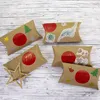 Several brown pillow boxes decorated with Christmas-themed stickers and numbered circles, arranged on a light wooden surface. Produktbild-Vorschau