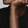 A close-up shot of a person's arm wearing a gold bracelet with a dangling charm. Podgląd zdjęcia produktu