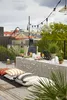 A rooftop party setup with string lights, a table with food and drinks, and floor cushions. Náhled obrázku produktu