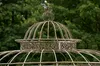 Close-up of the ornate top of a metal garden structure, likely a gazebo or birdcage, with a leafy background. Anteprima dell’immagine prodotto