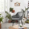 A gray velvet chair with black metal legs is placed in a room with several potted plants and a decorative sign. Produktbild-Vorschau