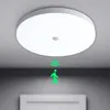 A white ceiling light fixture with a motion sensor is shown mounted on a ceiling. A green graphic overlay depicts a person walking and motion waves emanating from the sensor, indicating its functionality. Náhľad obrázku produktu