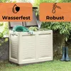 A garden storage box filled with garden hoses and gardening tools, placed outdoors on grass next to a wall and trees. Two pairs of rubber boots are visible on the right. Produktbild-Vorschau