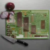 A cutting board shaped like a motherboard with onions and a knife on a metallic surface. Produktbild-Vorschau