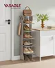 A tall, narrow shoe rack with several shelves, holding various pairs of shoes and a handbag on top. An umbrella is hanging from a hook on the side. A vase with flowers and some books are on a cabinet in the background. Produktbild-Vorschau