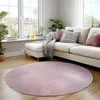 A round pink rug in a living room with a sofa and plants.