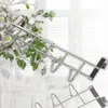 A silver metal over-the-door hook rack with multiple hooks, set against a blurred background of greenery and white curtains. Produktbild-Vorschau