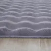 A close-up, low-angle view of a fluffy, gray rug with a wavy texture, lying on a wooden floor. Produktbild-Vorschau