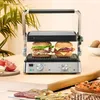 A grill with two burgers being cooked, surrounded by ingredients and food. Podgląd zdjęcia produktu