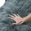 A hand is pressing into a soft, plush, dark gray blanket. Produktbild-Vorschau