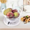 A kitchen scale with fruit in a clear bowl, placed on a wooden surface, with a colander and kitchenware in the background. Voir les images du produit