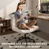 A woman sits cross-legged in a modern office chair, reading a magazine. The scene includes a desk, shelves, and a rug. Produktbild-Vorschau
