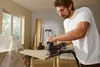 A man is using a jigsaw to cut a piece of wood in a workshop. Produktbild-Vorschau
