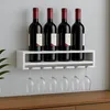 A white wine rack with four wine bottles and six wine glasses hanging from it, placed on a wooden surface against a light gray wall. Podgląd zdjęcia produktu
