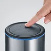 A finger is pressing a button on the lid of a stainless steel appliance with a blue accent ring. Produktbild-Vorschau