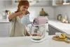 A woman is pouring liquid into a stand mixer in a kitchen. Voir les images du produit