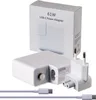 A white USB-C power adapter and its accessories are displayed on a white background, with the product's packaging in the background. Podgląd zdjęcia produktu