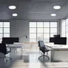 A modern office space with large windows, desks, and chairs, illuminated by ceiling lights. Produktbild-Vorschau