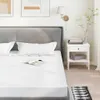 A bed with white sheets and pillows, a nightstand with books and a lamp, and artwork on the wall. Voir les images du produit