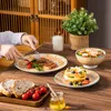 A table setting with plates of food, bread, and a salad, with hands cutting into a steak. Produktbild-Vorschau