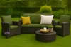 A patio furniture set including a sofa, two chairs, and a coffee table, arranged on a grassy lawn with a hedge in the background. Produktbild-Vorschau