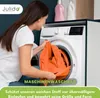 A woman is putting orange fabric into a washing machine. Produktbild-Vorschau