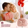 A couple embracing, with a gift box and balloons in the background, and a pink chair in the foreground. Produktbild-Vorschau