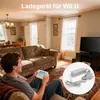 A man is playing a video game on a couch in a living room, with a charger for the game console shown in a circular inset. Produktbild-Vorschau