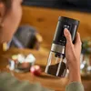 A person is holding a black and silver electric coffee grinder with a glass container filled with coffee grounds. Produktbild-Vorschau