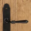 A close-up shot of a black door handle and escutcheon plate mounted on a wooden door. Produktbild-Vorschau