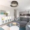 A modern living room and kitchen area with a sectional sofa, coffee table, and a decorative ceiling light. Produktbild-Vorschau