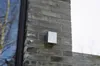 A silver cube-shaped outdoor light fixture mounted on a gray brick wall next to a window. Voir les images du produit